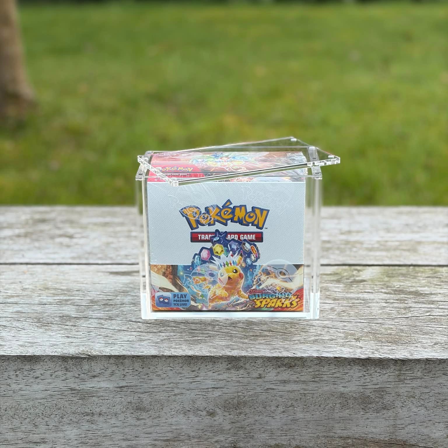 Pokémon trading card game box on a wooden surface with a grassy background